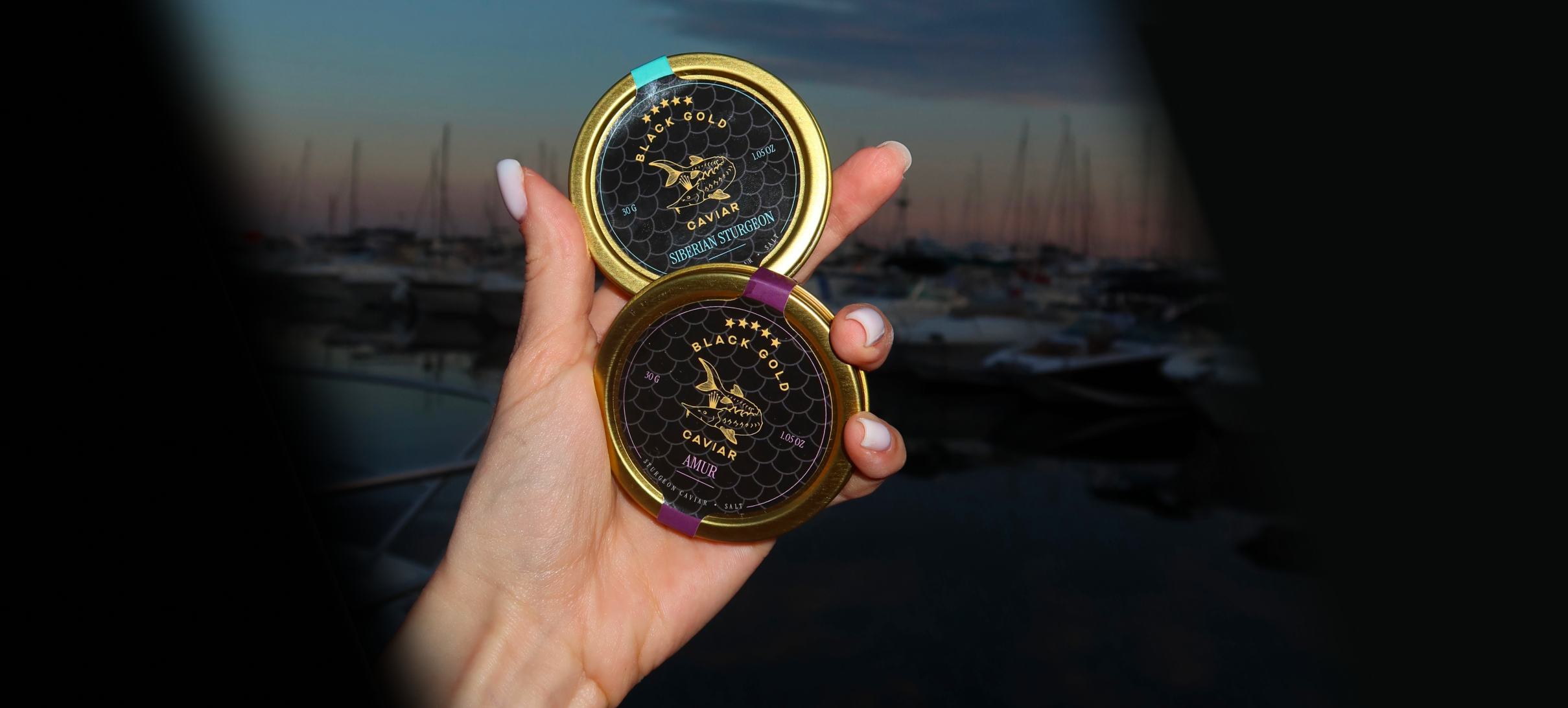 Black Gold Caviar Amur — premium black sturgeon caviar tins held at luxury marina at sunset, ideal gourmet gift available with overnight shipping in the USA.